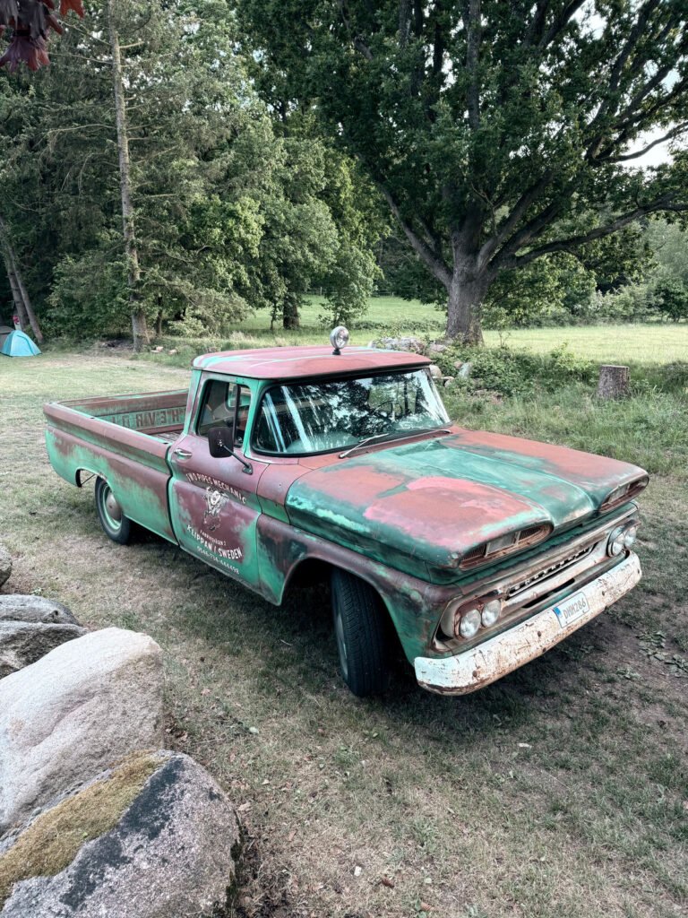 Ein alter, rostiger, grün-roter Pickup mit verblasster Farbe ist auf dem Rasen in der Nähe von Bäumen und Felsen in einer ländlichen Umgebung geparkt.